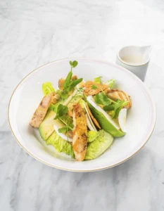 A Caesar salad with grilled chicken, parmesan cheese, avocado, and a Caesar dressing.